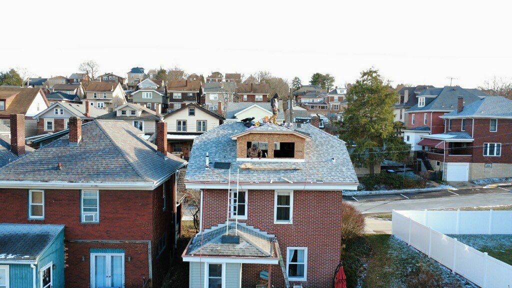 Drone view of a brick home with a new shed dormer framed into the existing shingle roof