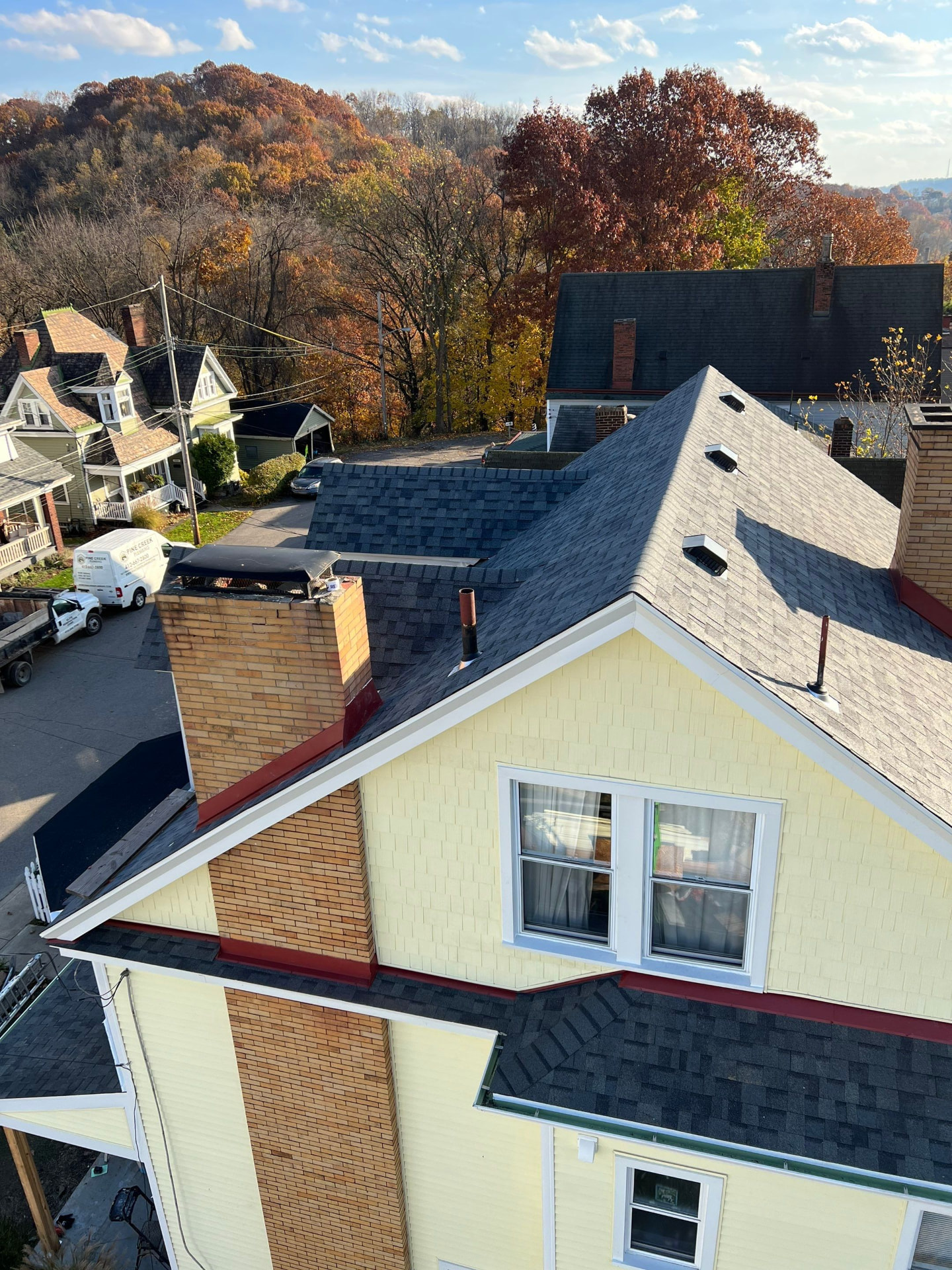 New shingle roof and red chimney flashing on a yellow Pittsburgh home in autumn