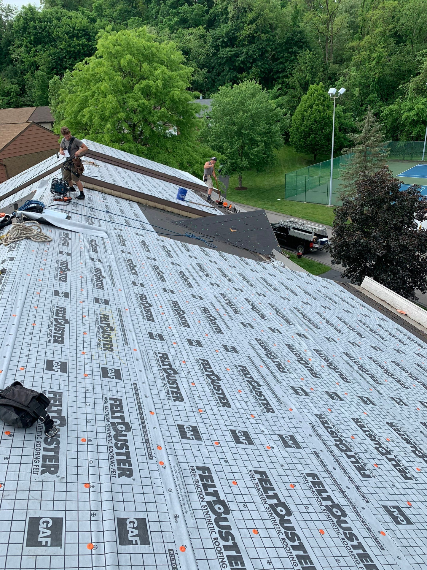 Two roofers installing GAF FeltBuster synthetic underlayment across a large sloped roof