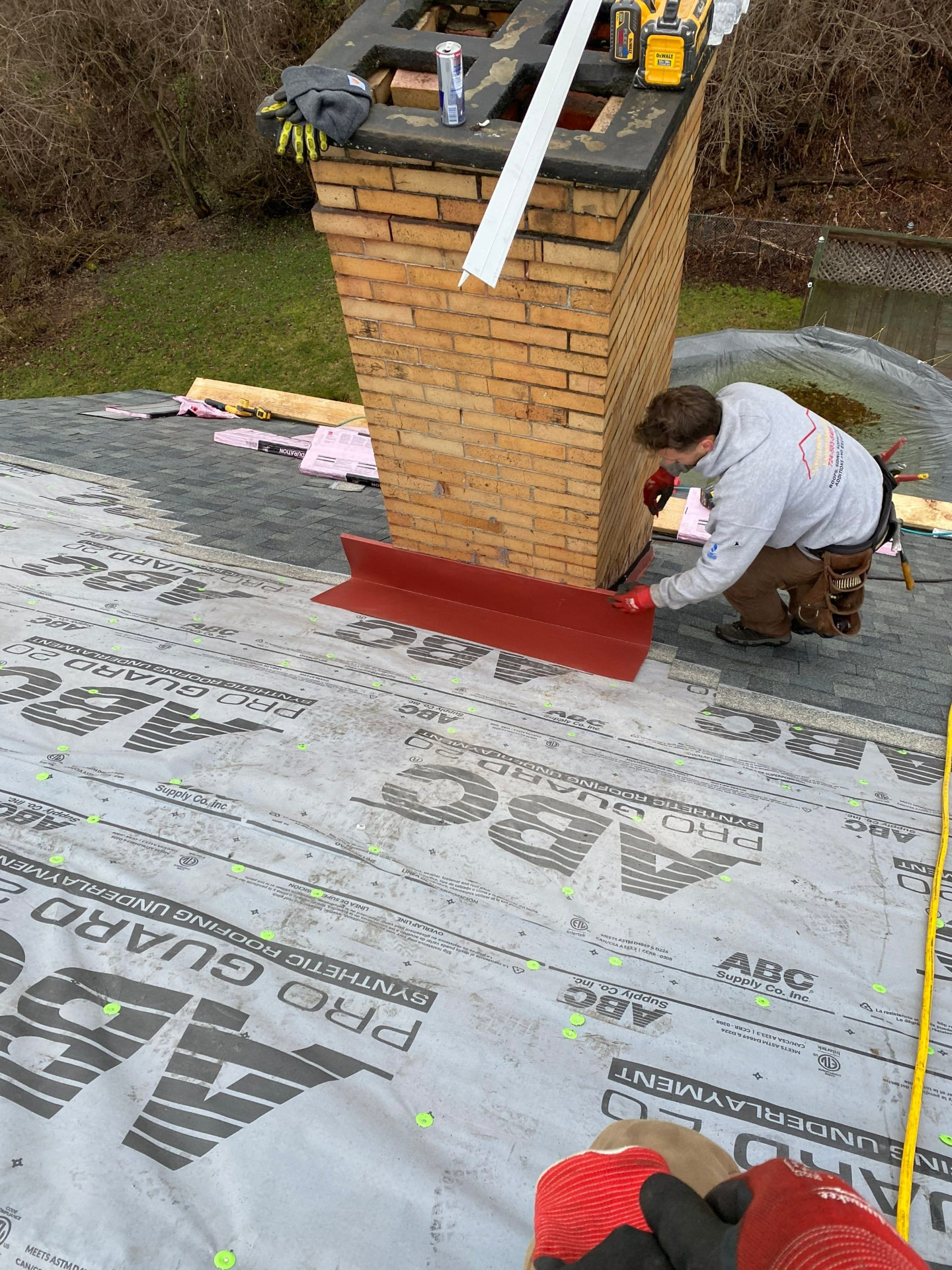 Roofer setting red painted chimney flashing over ABC Pro Guard synthetic underlayment