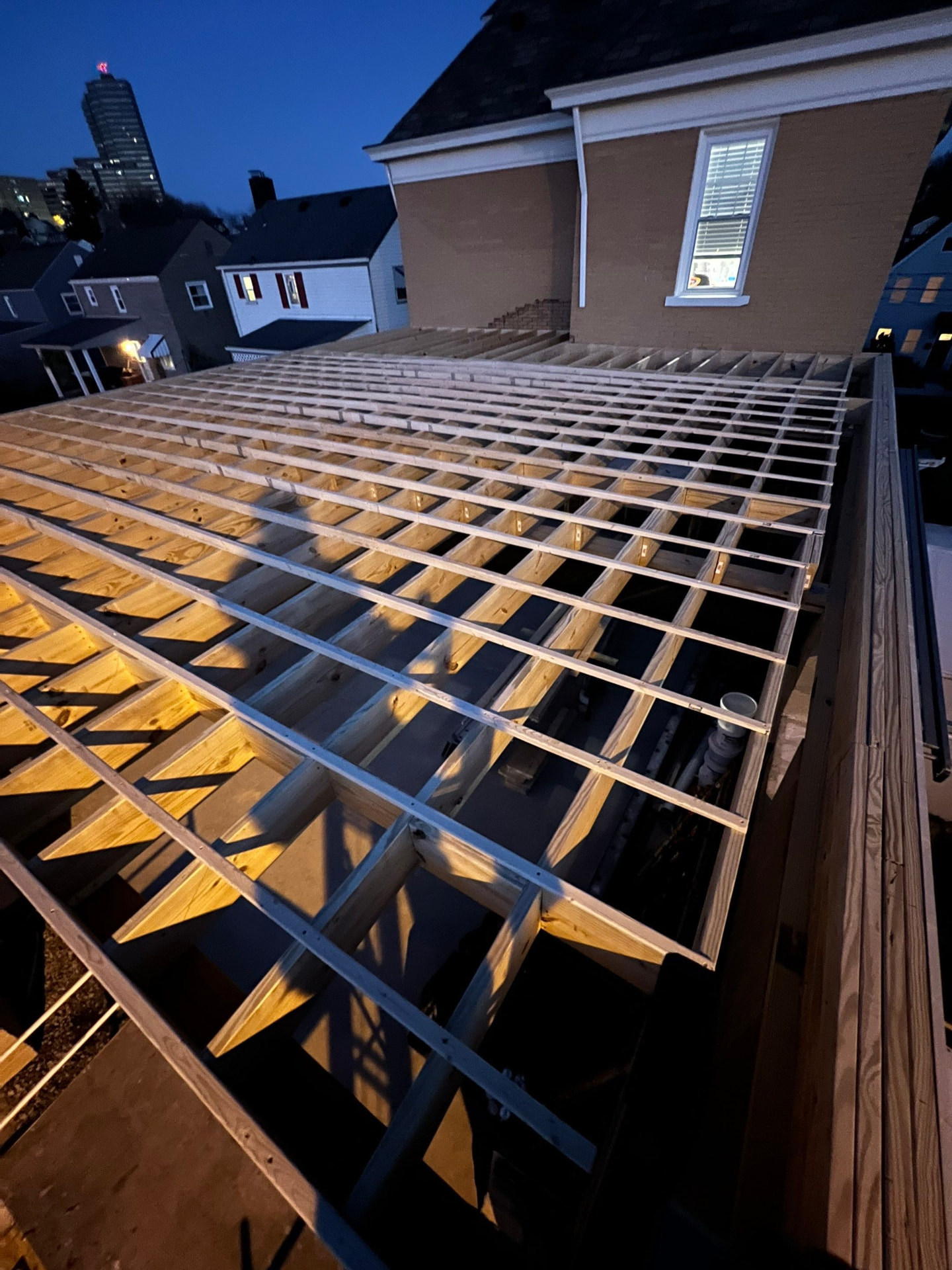 Night view of new deck joists and steel framing over a city rooftop addition