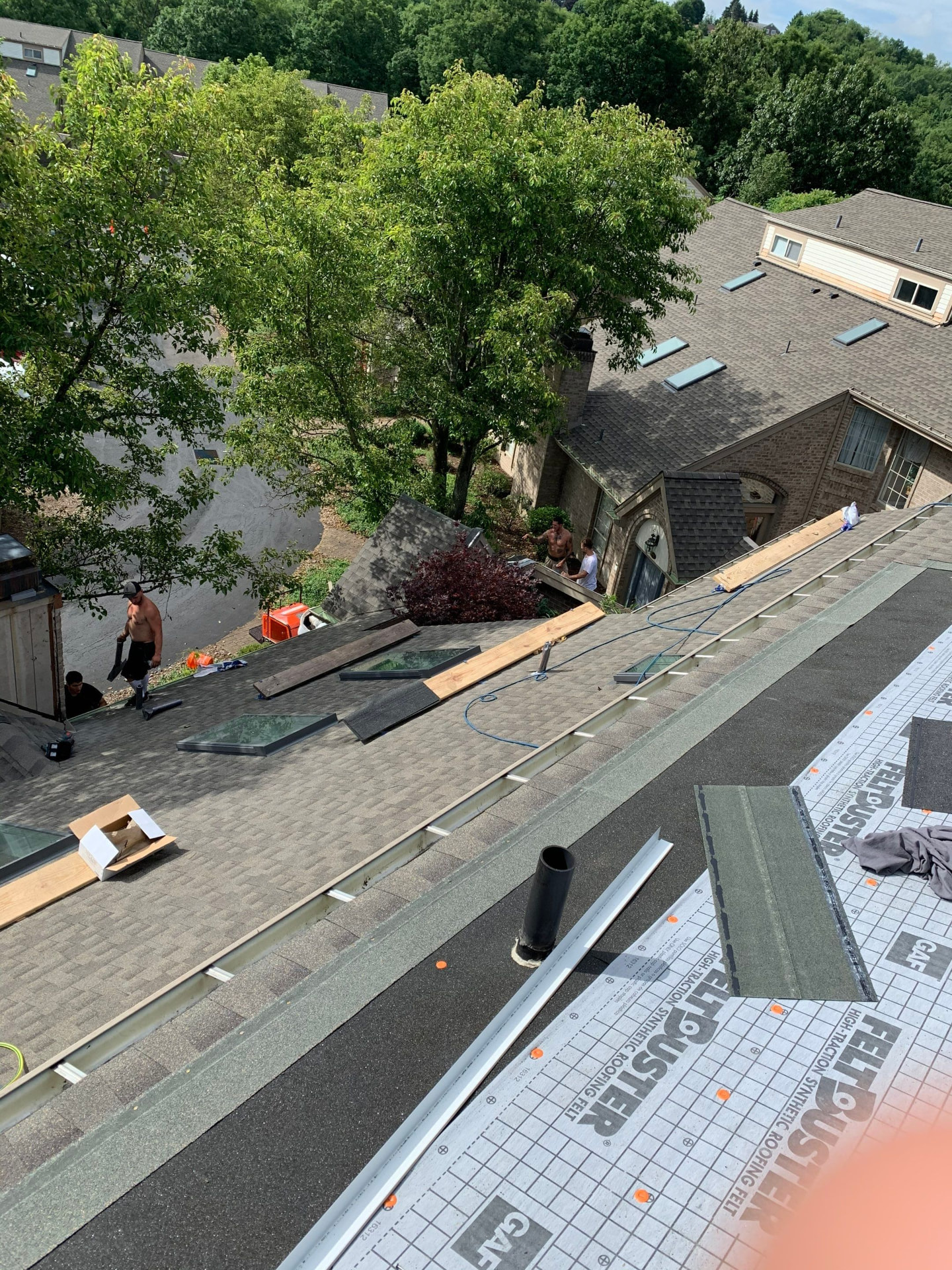 Crew installing skylights and ridge material on a large residential shingle roof