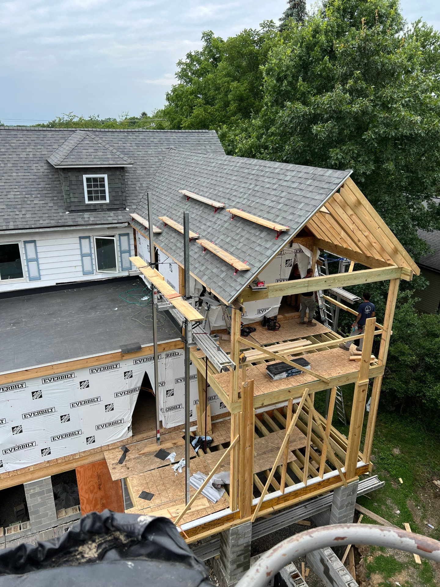 Crew framing a covered porch addition with new gable roof and pressure-treated posts