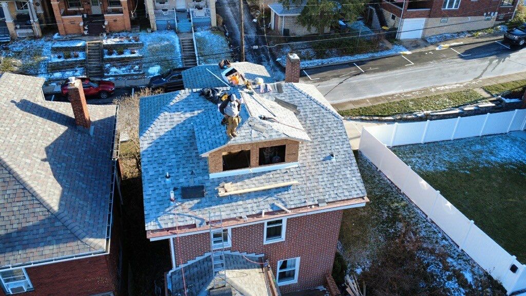 Winter aerial of a brick home with a new dormer opening framed and shingles going on