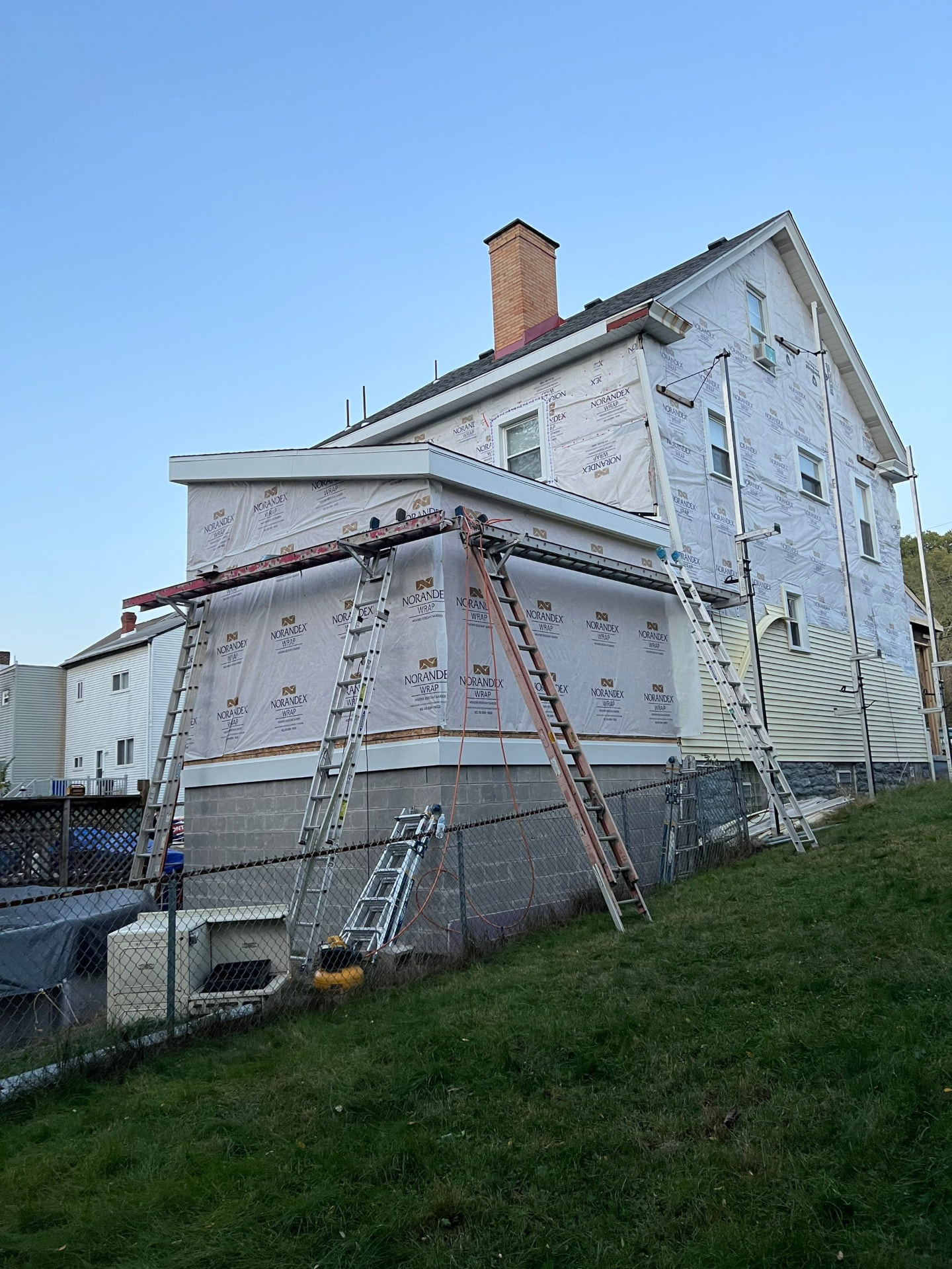 Home fully wrapped in weather barrier with ladders and staging ready for new siding
