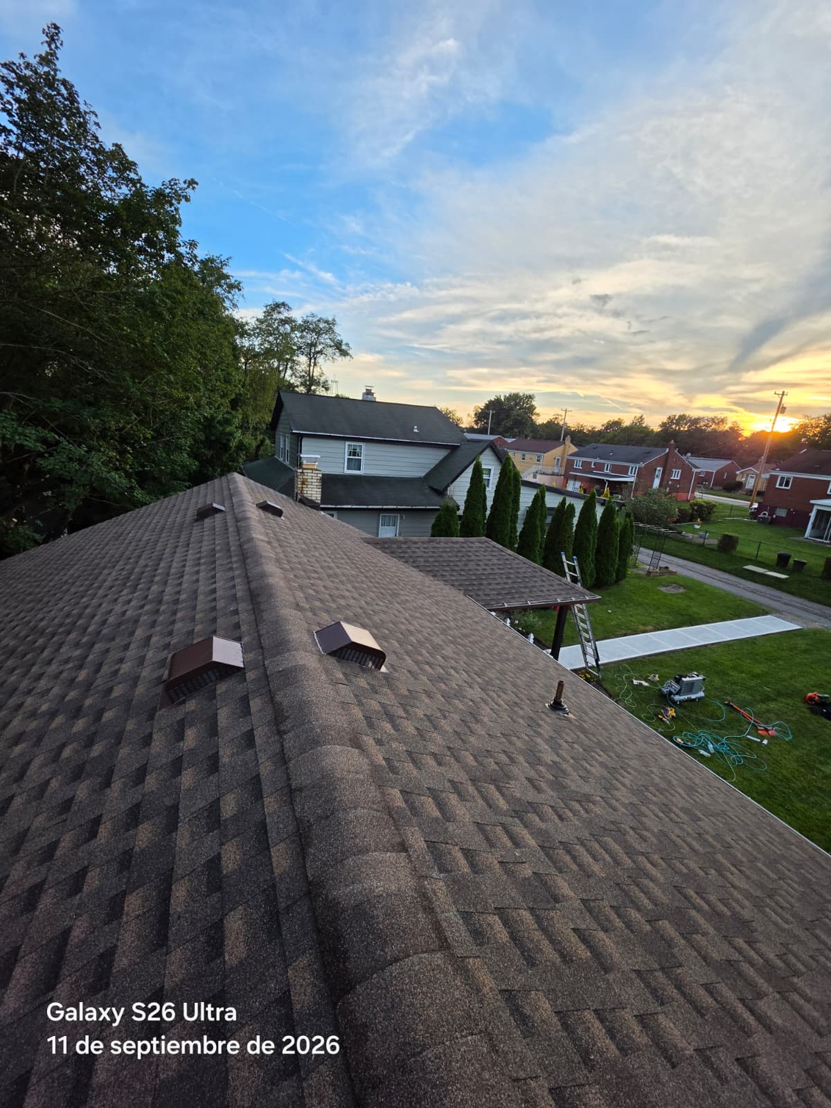 High-angle view along a roof ridge with four box vents installed and a sunset over the neighborhood