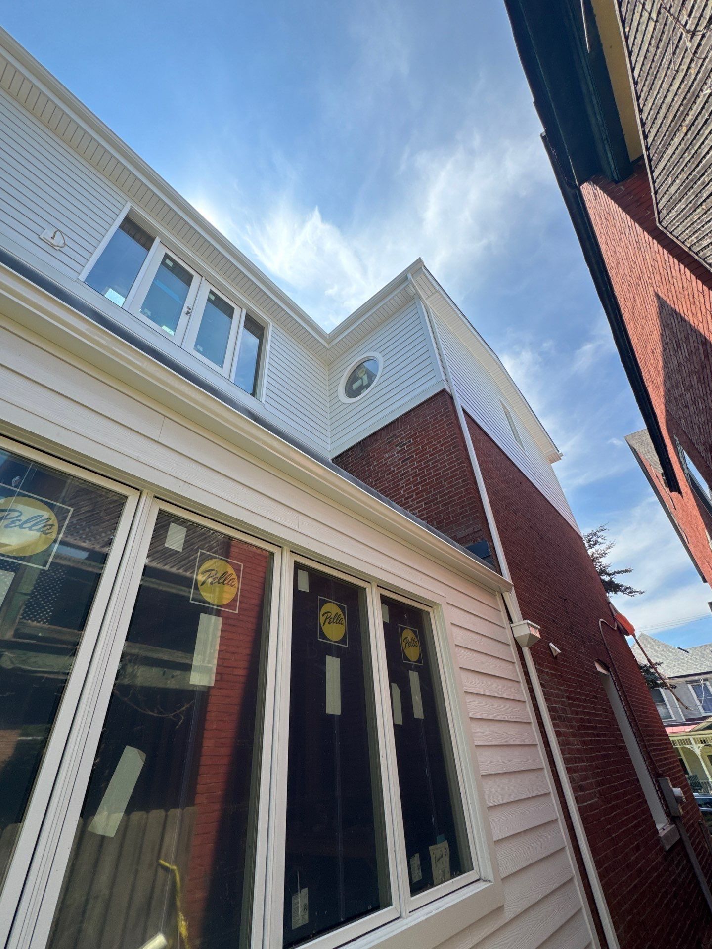 New white lap siding and gutter work on a city home dormer against blue sky
