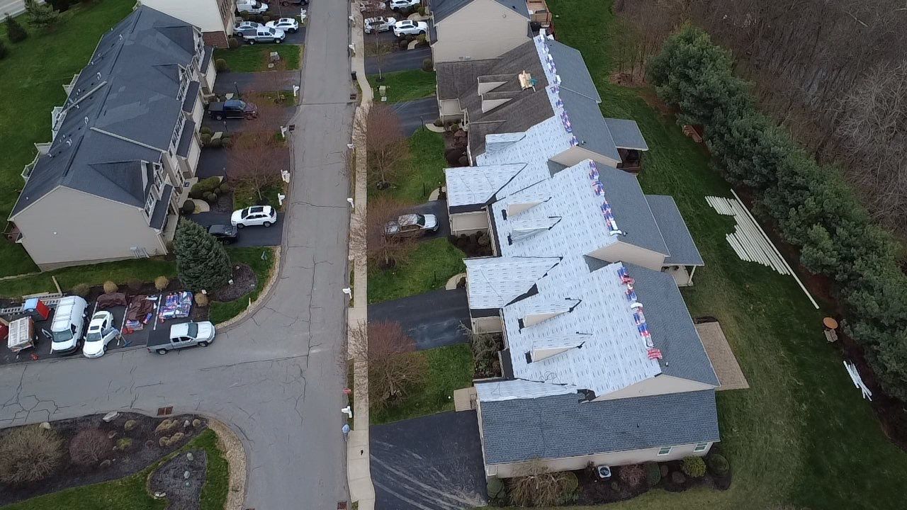 Aerial view of a townhome row with synthetic underlayment down and shingle bundles staged on the roof