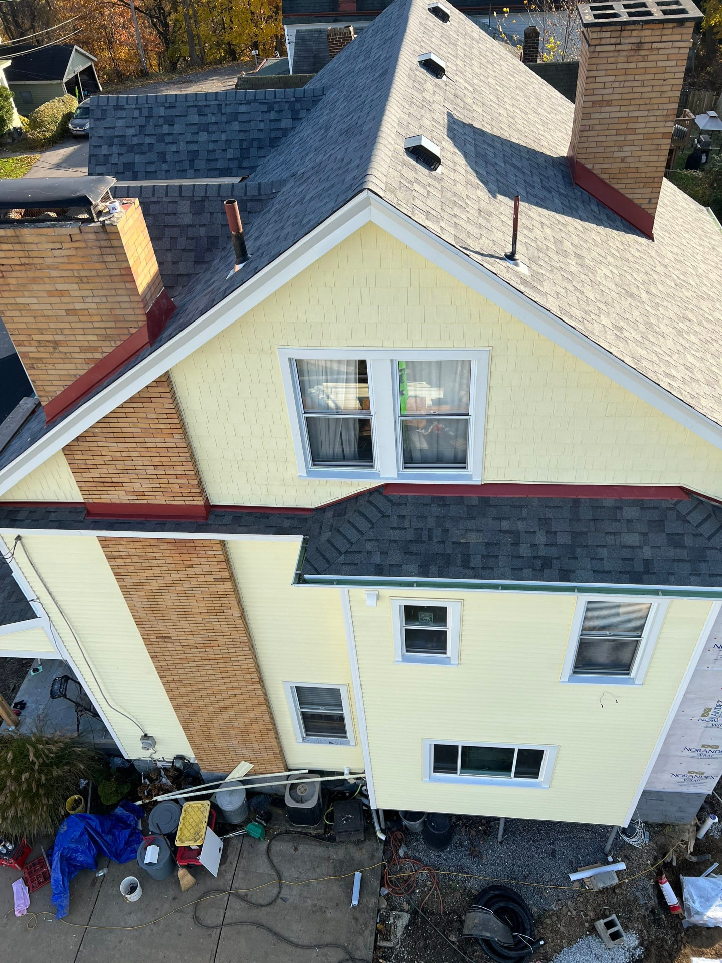 Aerial view of a yellow-sided home with new architectural shingles, red flashing and brick chimneys