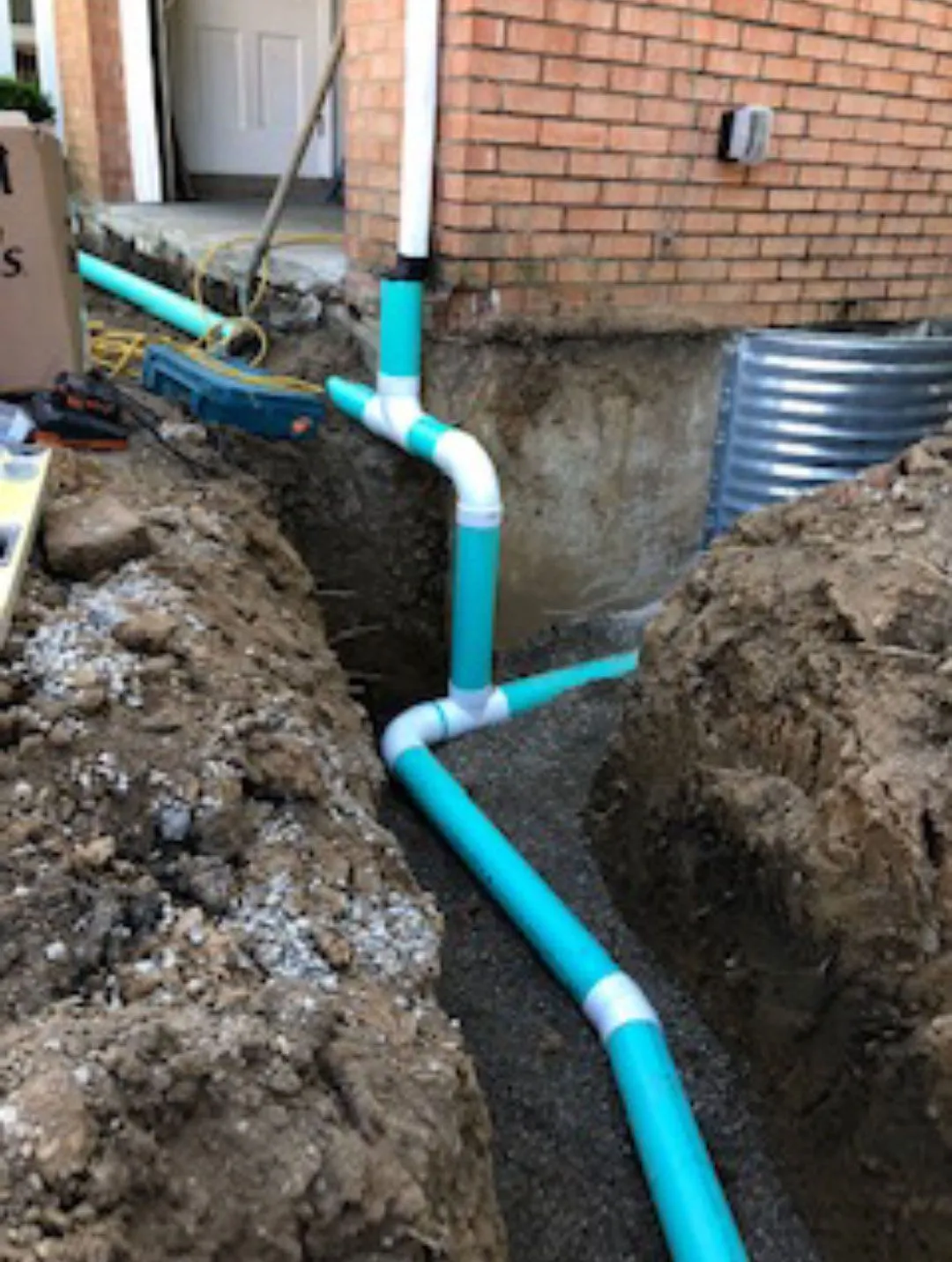 Buried downspout piping trenched alongside a brick home and tied into an underground drain line