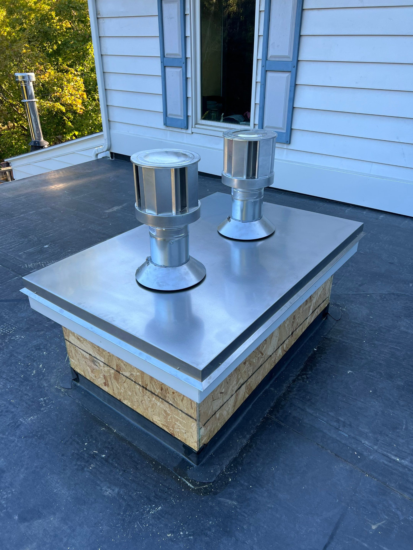 Finished EPDM flat roof with new metal-capped vent curb and stainless chimney caps