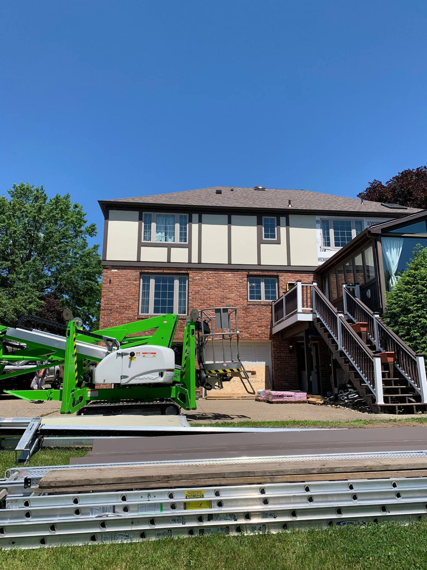 Tudor-style home with new stucco panel siding, trim stock staged and a spider lift on site