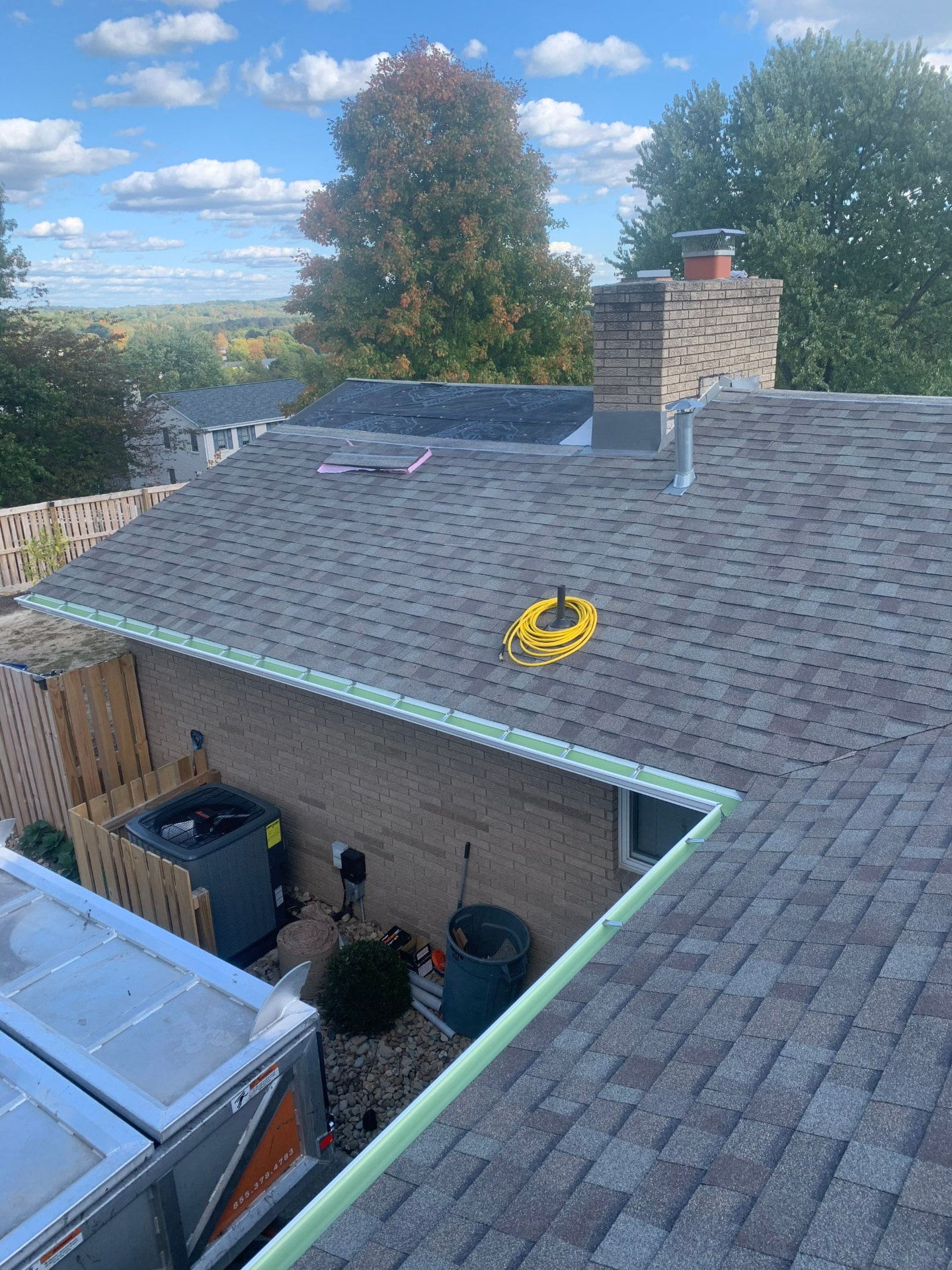 Completed shingle roof with new white gutters, chimney flashing and flat roof section