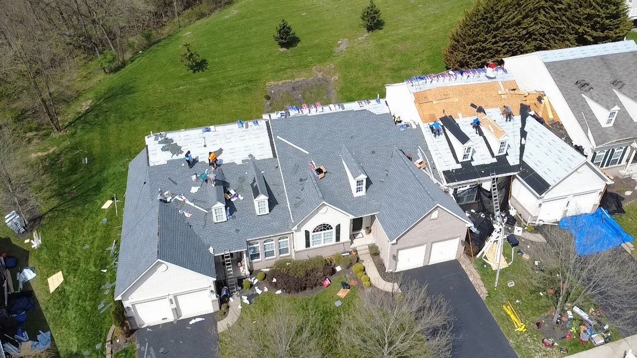Aerial view of a large suburban home mid re-roof with crew laying underlayment and shingles