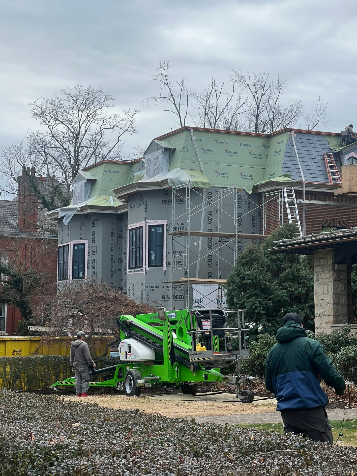 Historic home with slate roof replacement underway behind scaffolding and underlayment