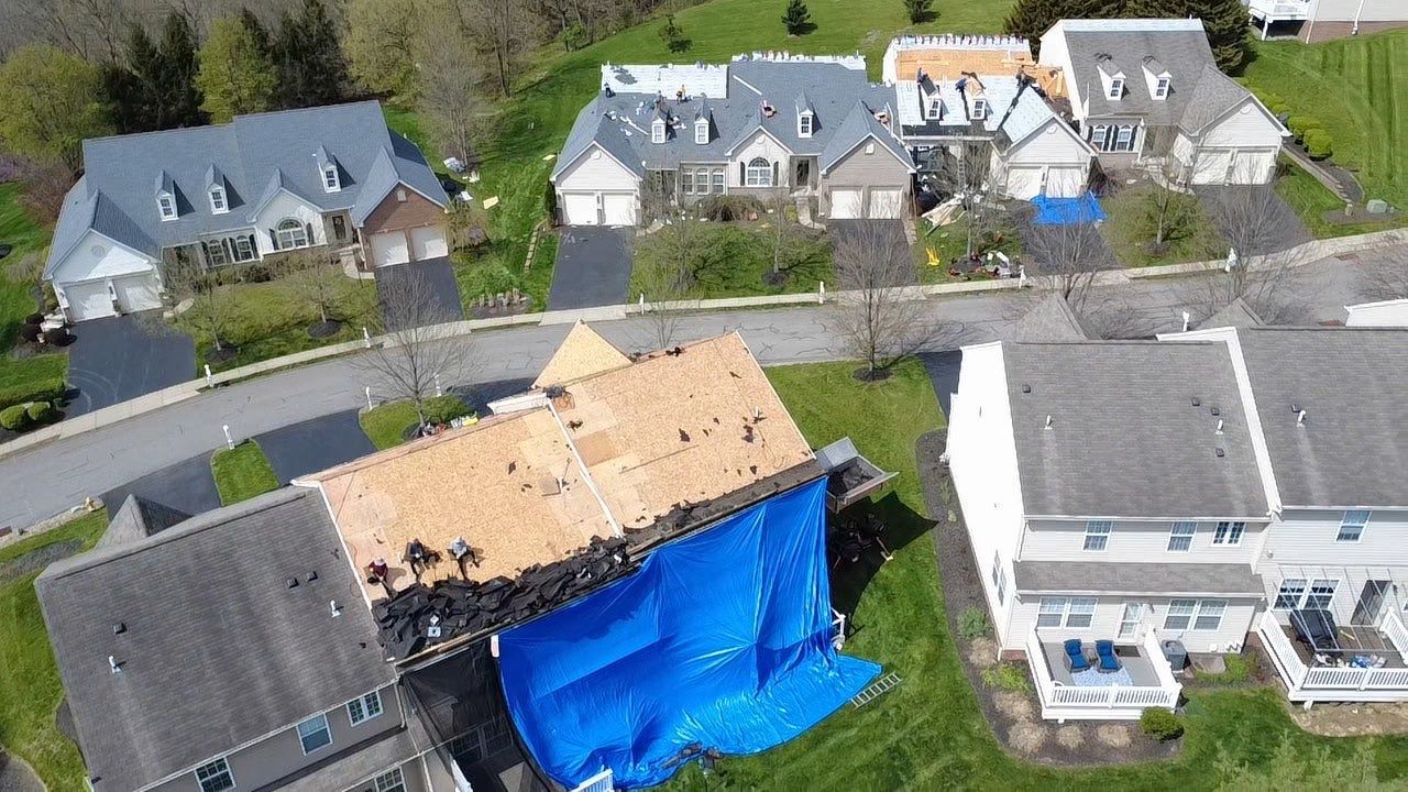 Aerial view of a townhome community tear-off with blue tarp protection and exposed decking