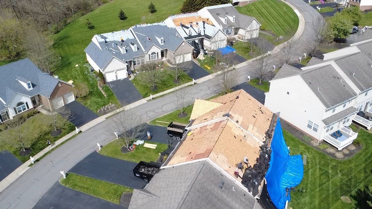 Aerial view of a residential tear-off with dump trailers and tarps protecting the yard