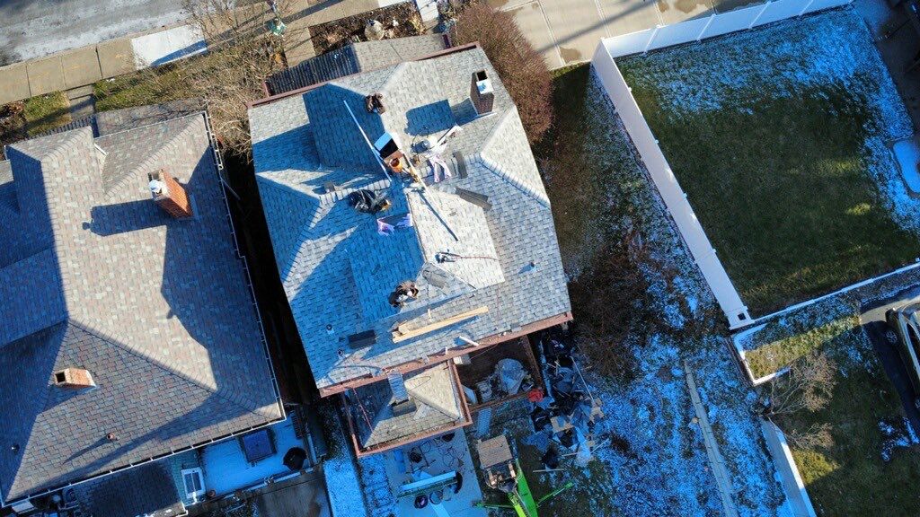 Winter drone view of a crew installing shingles on a city home roof