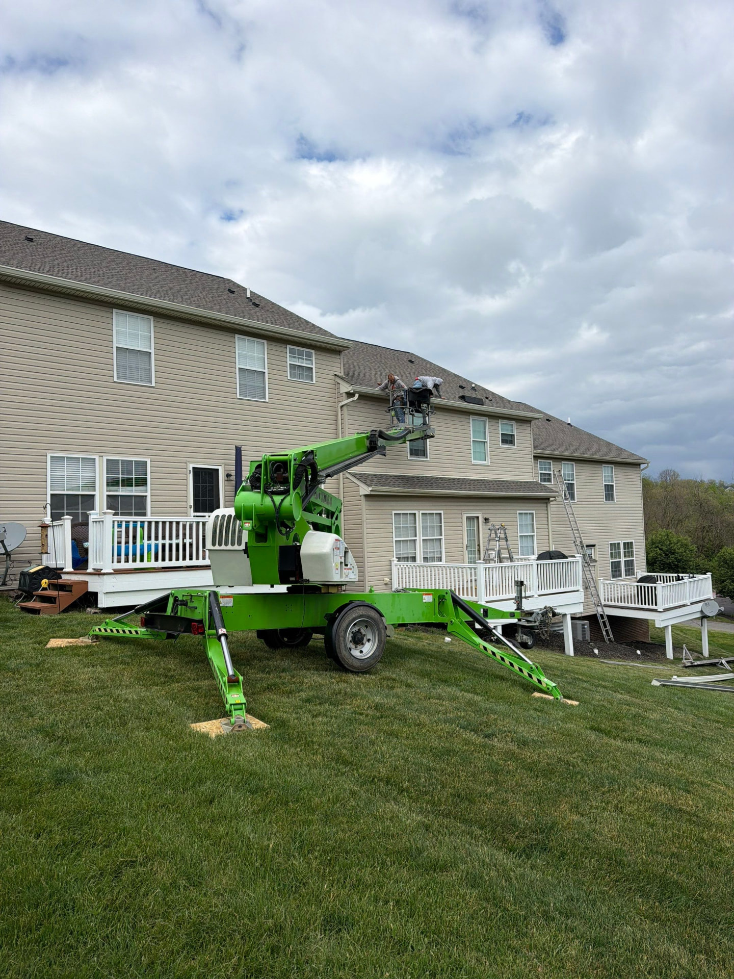Green spider lift positioned in a backyard while crew installs gutters along the roof edge
