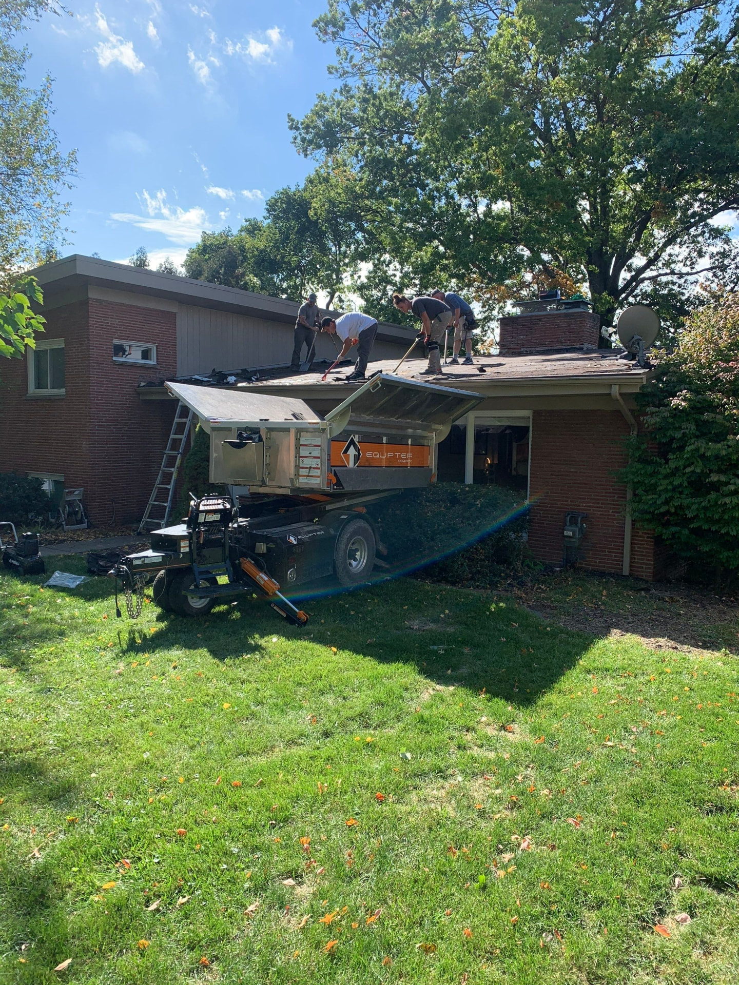 Roofing crew tearing off old shingles into an Equipter lift on a brick ranch home