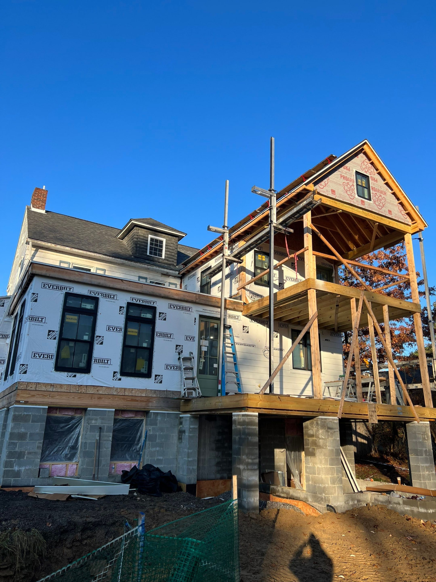 Two-story home addition framed with a covered porch structure and house wrap