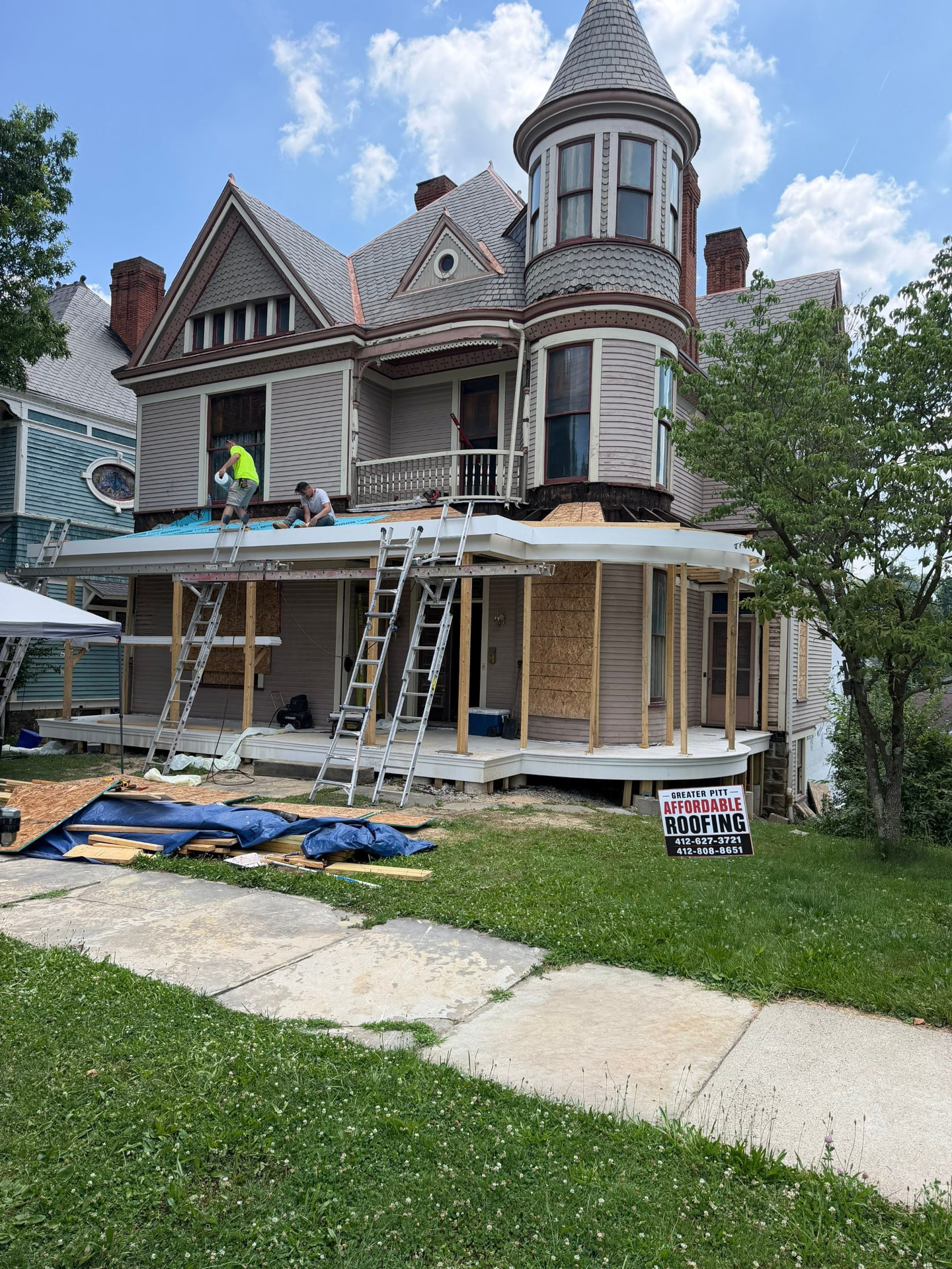 Crew rebuilding the wrap-around porch roof on a Victorian home with a Greater Pitt Affordable Roofing yard sign