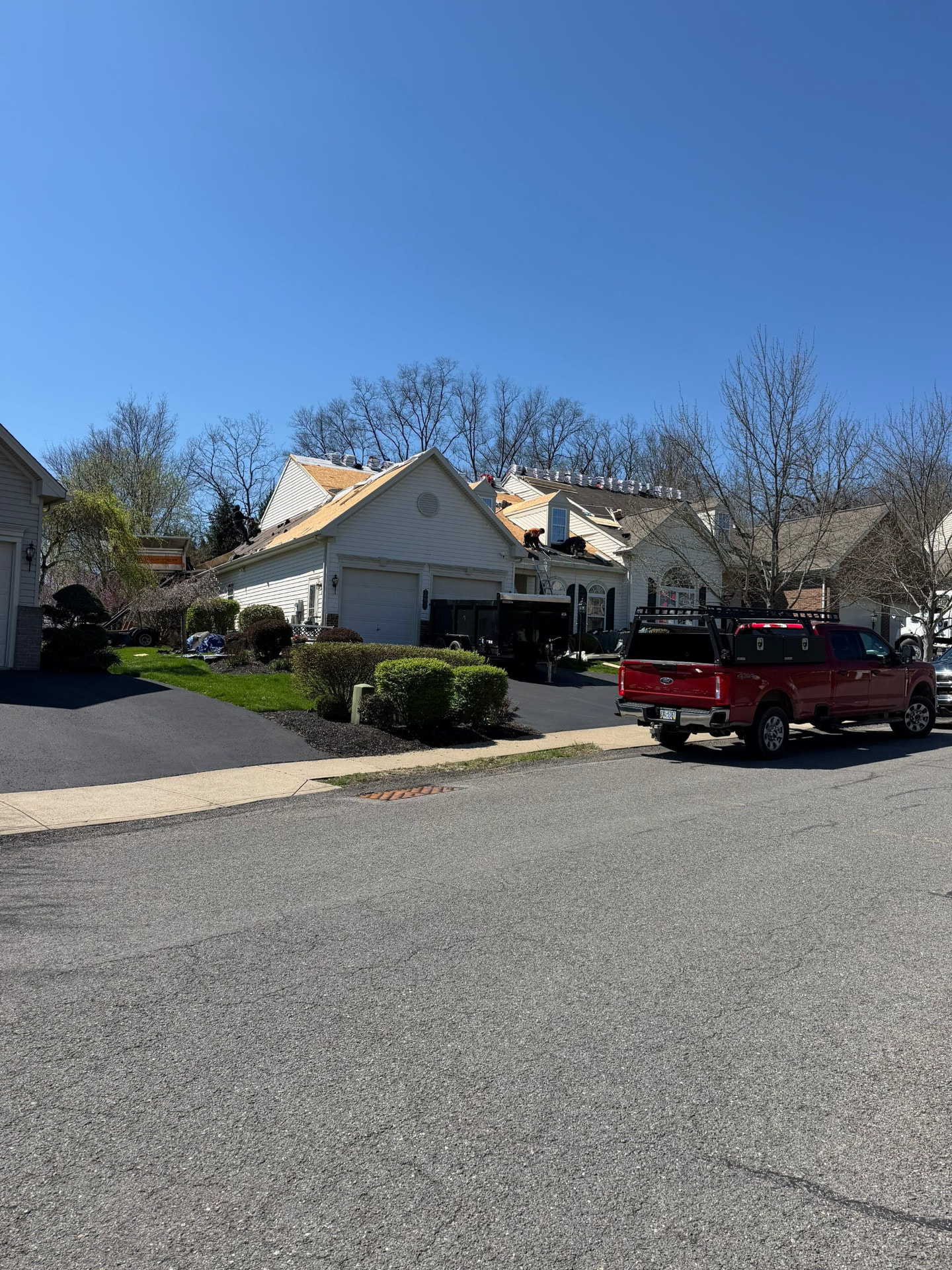 Crew re-roofing a residential home with shingle bundles staged along the ridge