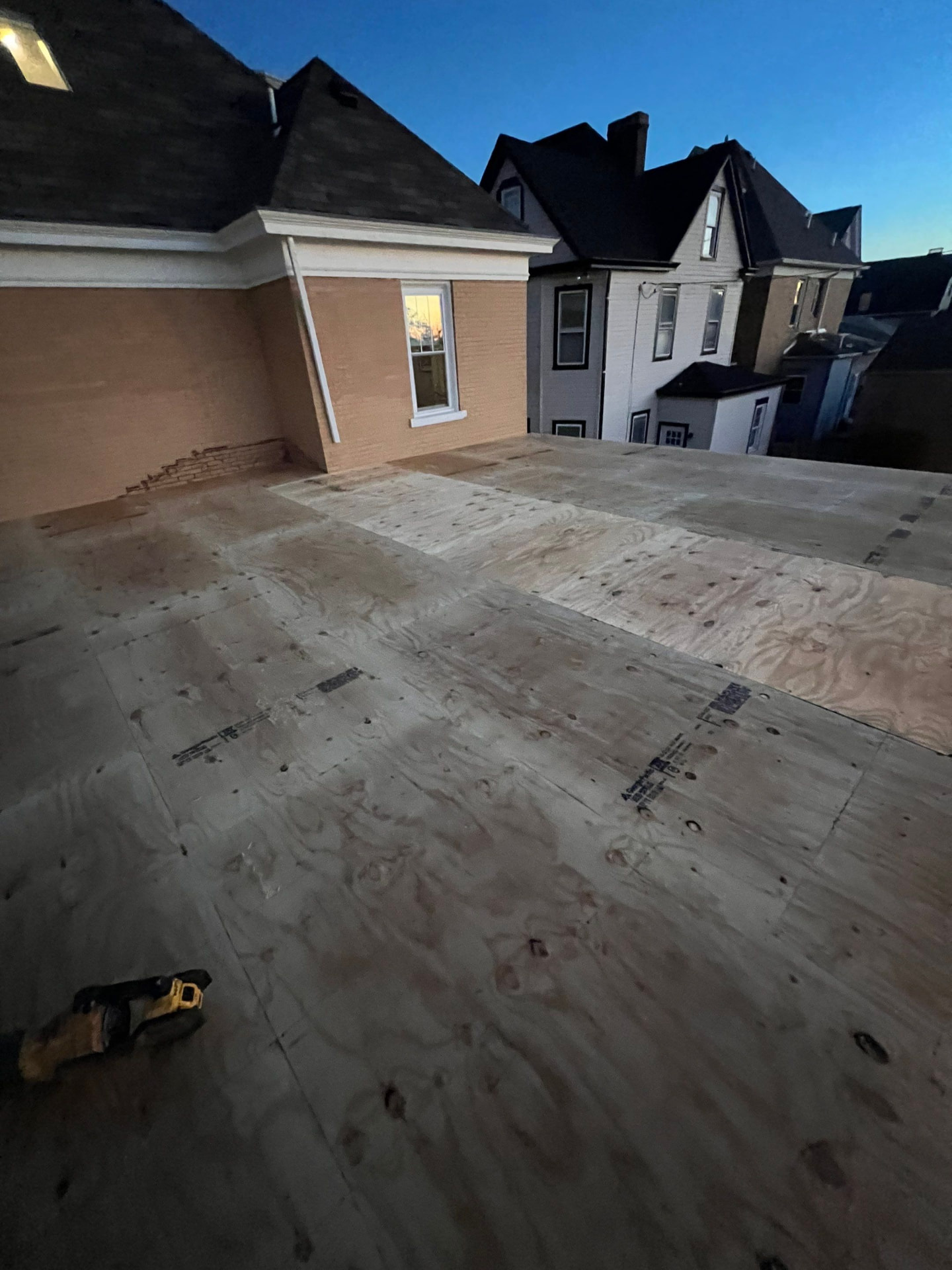 New plywood decking installed on a low-slope roof at dusk between two brick homes