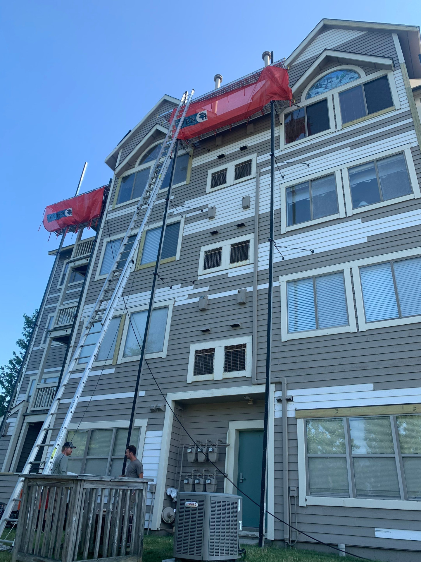 Four-story apartment building siding replacement with two swing-stage platforms and crew on site